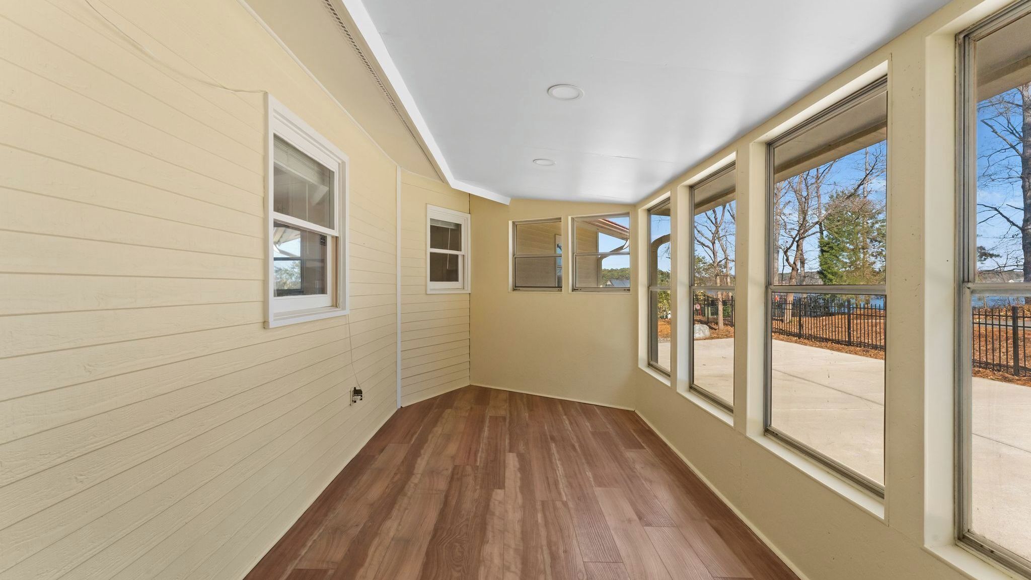 Un pasillo con suelo de madera, ventanas grandes y techo blanco.
