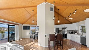 A spacious kitchen with white cabinets, a dining area with wooden chairs, and a view of a balcony with a railing. - Pleasant Cove Waterfront Getaway With Fire Pit, Deck, and Lake Views (Mooresville)