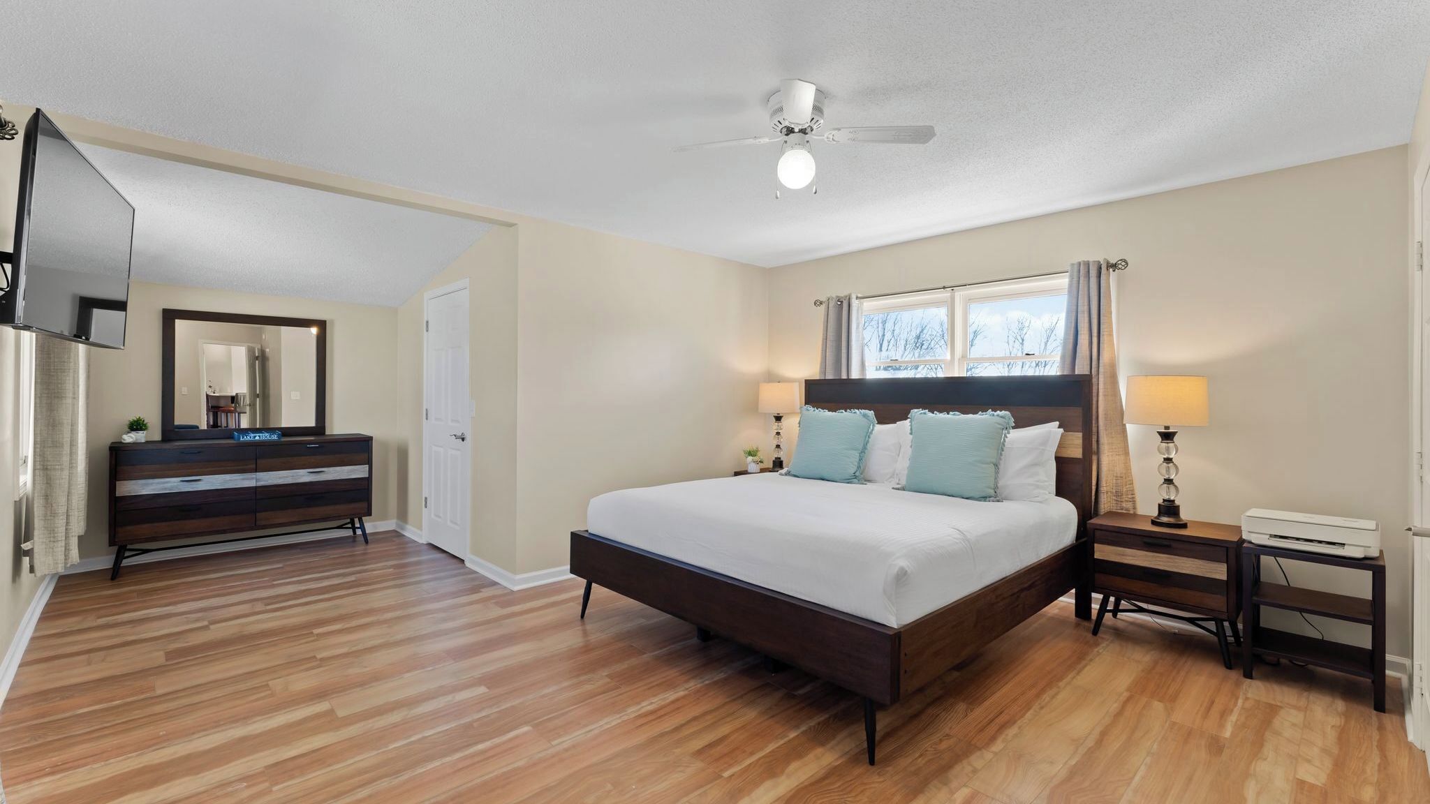 A bedroom with a bed, bedside tables, a dresser, a ceiling fan, and a TV.