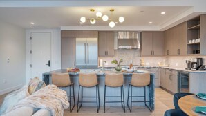 A modern kitchen with a central island, bar stools, a dining table, and a cozy seating area. - Alpine Oasis at Frontgate by Avantstay Luxe 3bdr Near Vail w/ Views Gym, Pool, Game Room (Avon)