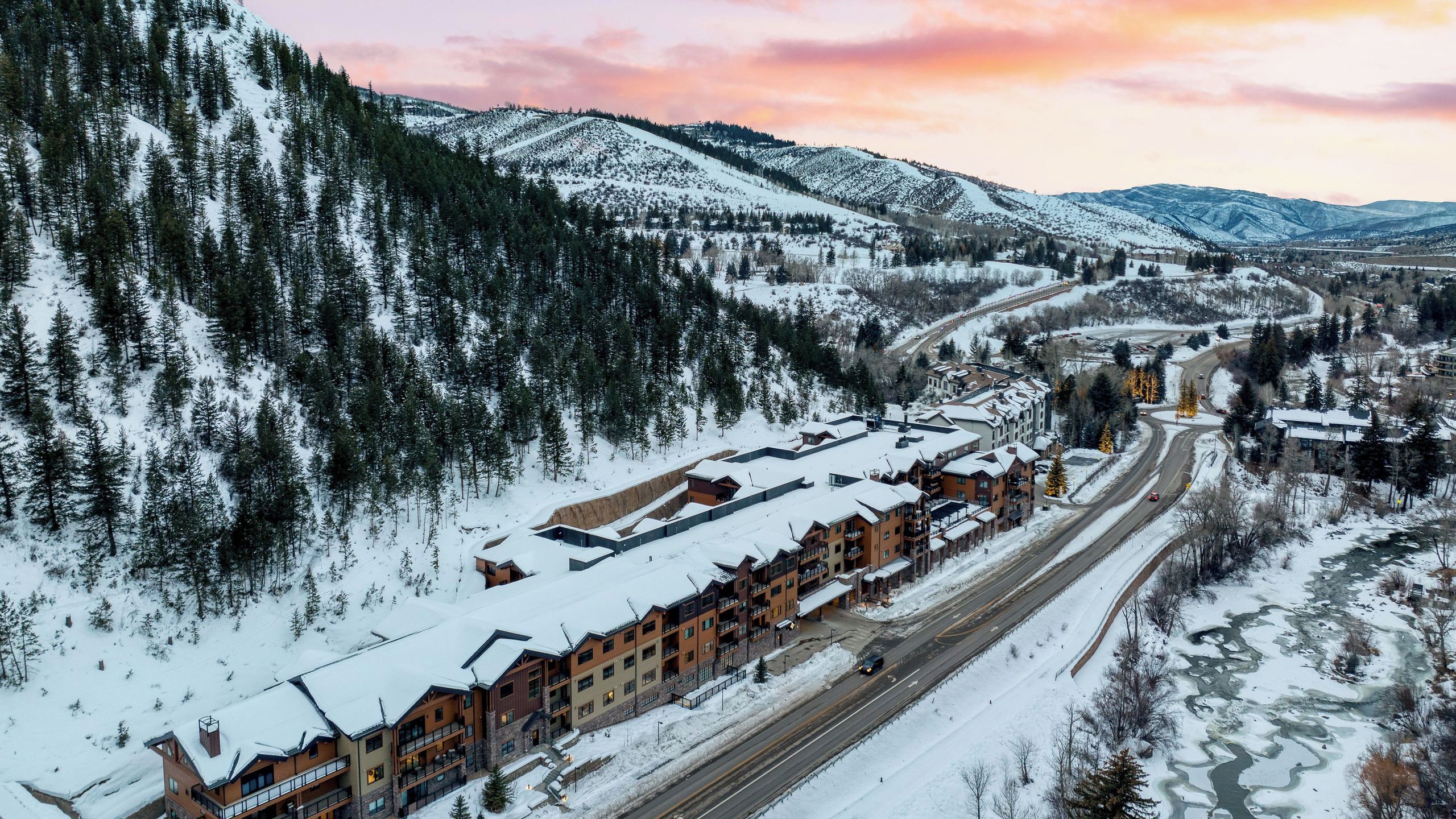 A snow-covered mountain resort with multiple buildings, a winding road, and a river.