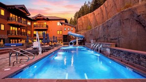 Une piscine avec un toboggan, des chaises longues et des parasols.