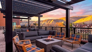 An outdoor patio with a fire pit, seating, and a view of a mountainous landscape. - Alpine Oasis at Frontgate by Avantstay Luxe 3bdr Near Vail w/ Views Gym, Pool, Game Room (Avon)