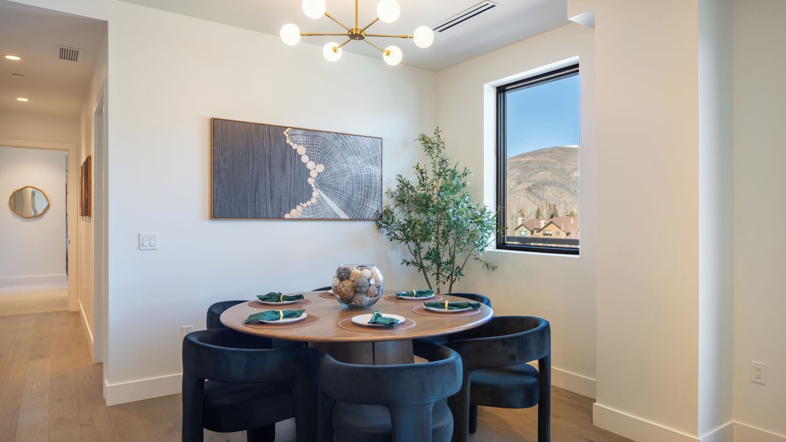 A dining area with a round table, black chairs, a vase, and a painting on the wall.