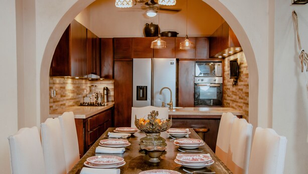 A dining area with a long table set for six, a chandelier, and a kitchen in the background. - Estrella de San Pedro by Zakher (Cartagena)