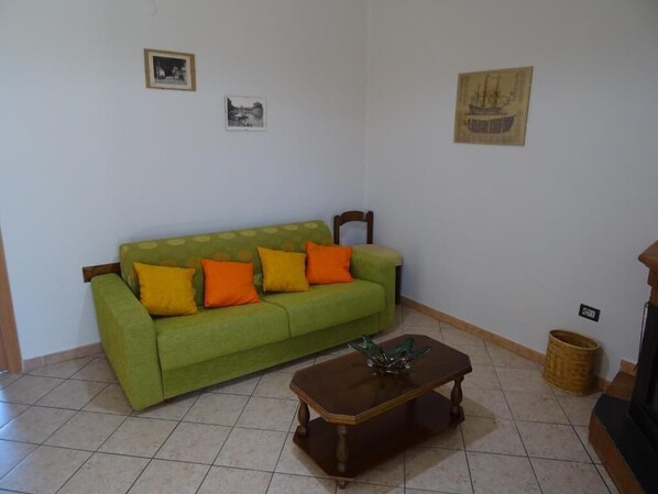 A living room with a green sofa, two orange cushions, a wooden coffee table, and a small basket. - Palazzo Marchesale (Novi Velia)