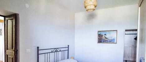 A bedroom with a bed, a nightstand, a hanging light, a painting, and a patterned floor.