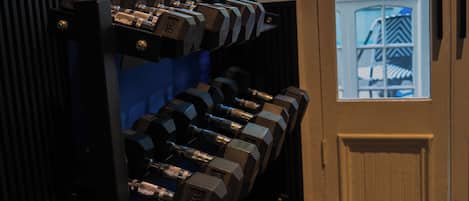 A row of dumbbells against a wall with a door and windows in the background.