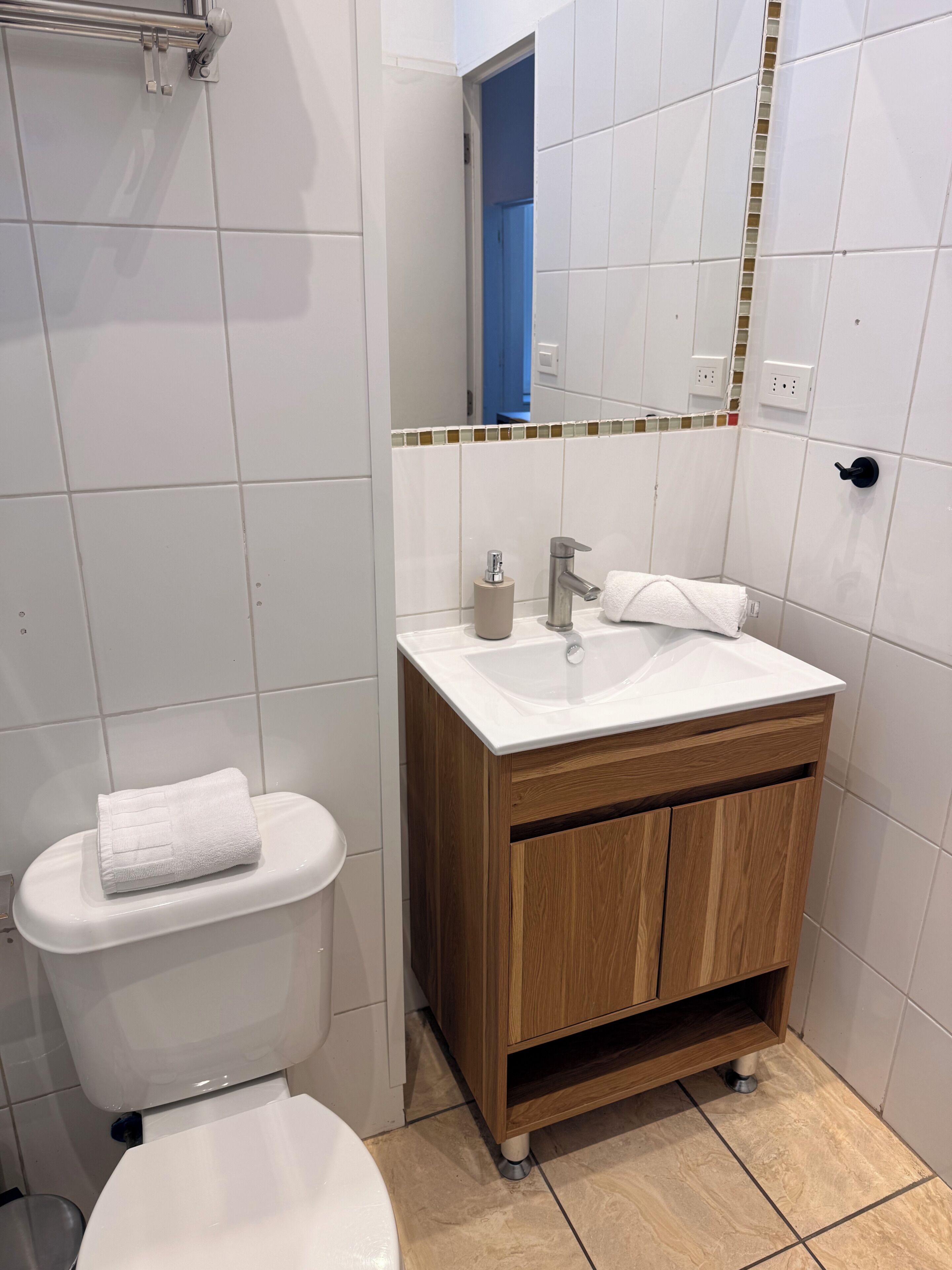 A bathroom with a white toilet, a wooden vanity with a sink, and a mirror above the vanity.