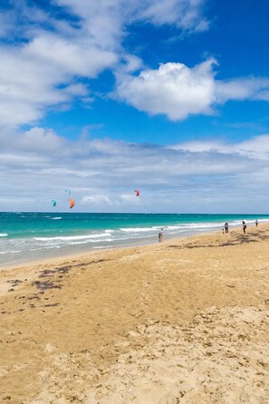 Una playa con cielos despejados, gente caminando y cometas volando.
