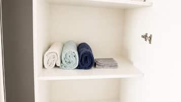 A white closet with shelves containing folded towels and a blue container.