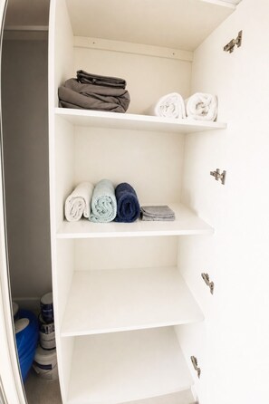 A white closet with shelves containing folded towels and a blue container.