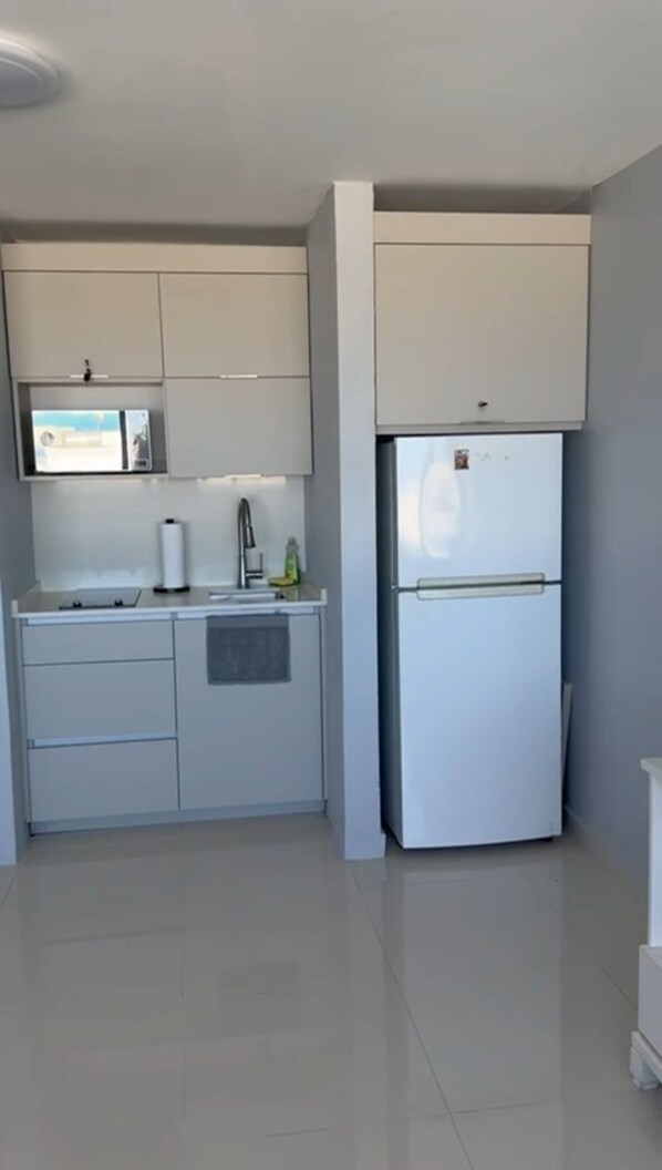 Una cocina compacta con armarios blancos, un microondas integrado y un refrigerador blanco.