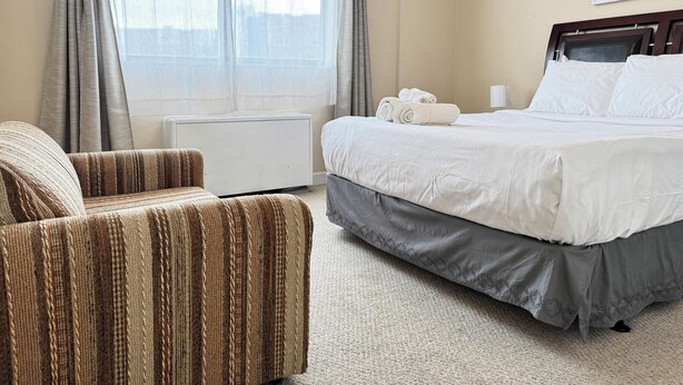 A hotel room with a bed, a chair, a radiator, and a window with curtains. - Downtown 3BD City View with Washer Dryer (Atlanta)