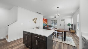Une cuisine moderne avec des meubles de couleur sombre, un îlot central blanc et un coin repas comprenant une table et des chaises en bois.