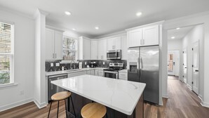 Une cuisine moderne avec des meubles blancs, un grand îlot central doté de tabourets, des appareils en acier inoxydable et un pare-feu noir et blanc.