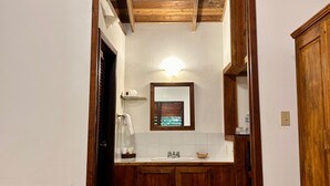 Ein schmaler Korridor mit Holzboden und Wandverkleidung aus Fliesen. Eine Holztür ist links, und ein Spiegel befindet sich an der Wand.