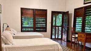 Ein Zimmer mit zwei Betten, Holzboden, Deckenventilator und großen Fenstern mit Holzläden.