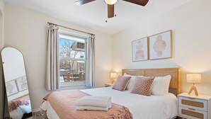 Ein Schlafzimmer mit einem großen Bett, einem Nachttisch mit Lampe, einem Spiegel und einem Fenster mit Vorhängen.