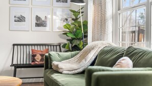 Ein grünes Sofa mit einer weißen Decke, ein Holztischchen, eine Zimmerpflanze und gerahmte Bilder an der Wand.