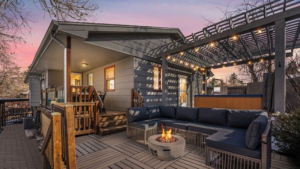 Eine überdachte Terrasse im Freien mit Feuerschale, einer Couch und einer Pergola mit Lichterkette.