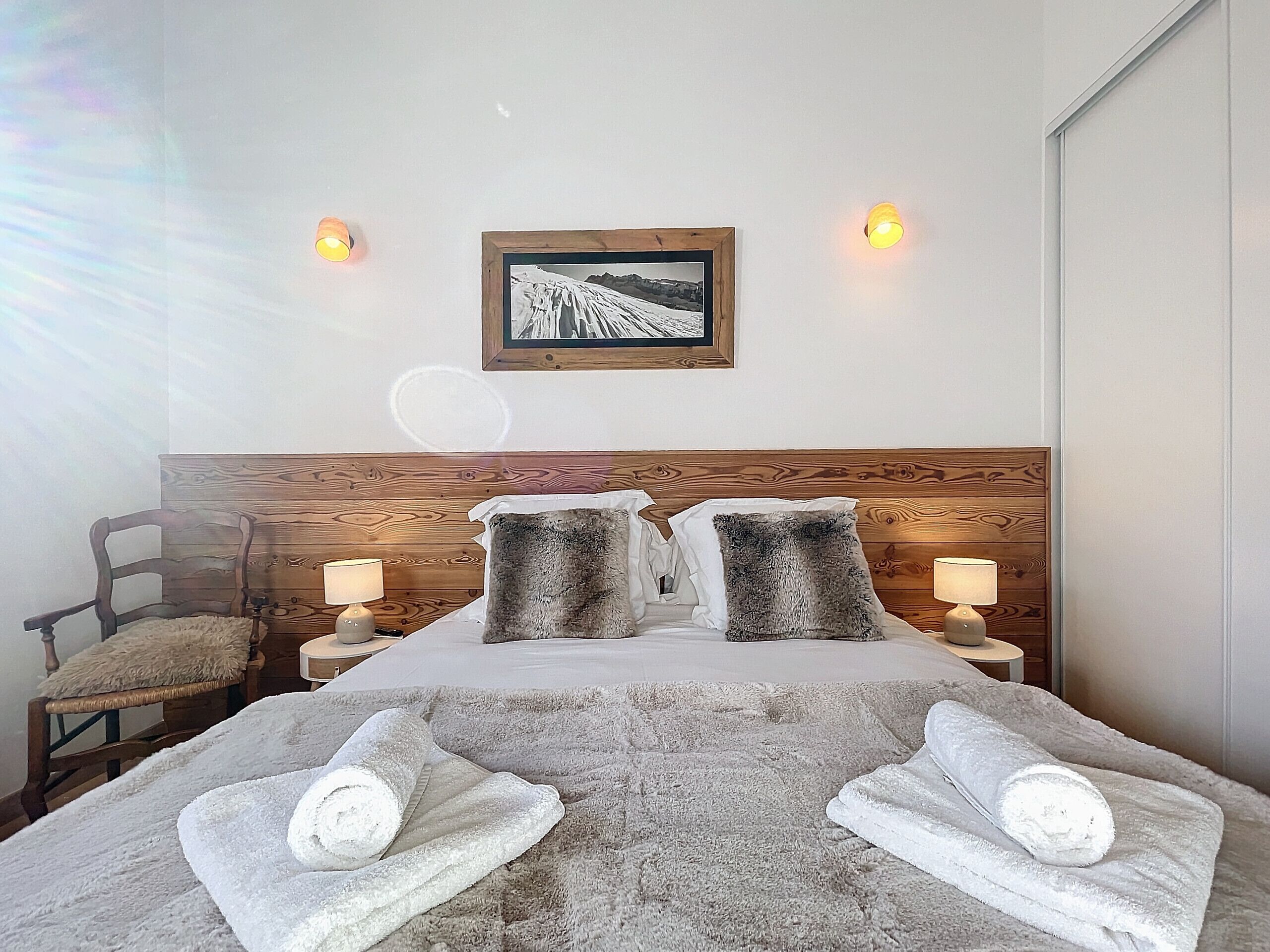 A hotel room with a wooden headboard, two bedside lamps, a framed picture on the wall, and two towels on the bed.