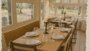 Un comedor con mesas y sillas de madera, velas y vistas a árboles a través de amplios ventanales.