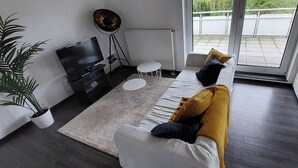 Ein modernes Wohnzimmer mit einer Couch, einem Fernseher, einer Stehlampe und einem Blumentopf.