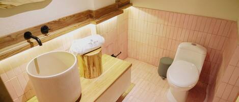 Un baño con tocador de madera, un lavabo grande, una toalla, un inodoro y un cubo de basura.