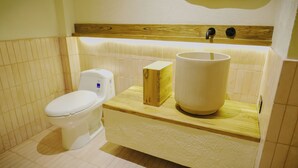 Ein Badezimmer mit Toilette, einem hölzernen Kasten und einem großen zylindrischen Behälter auf einer Holzeinrichtung.