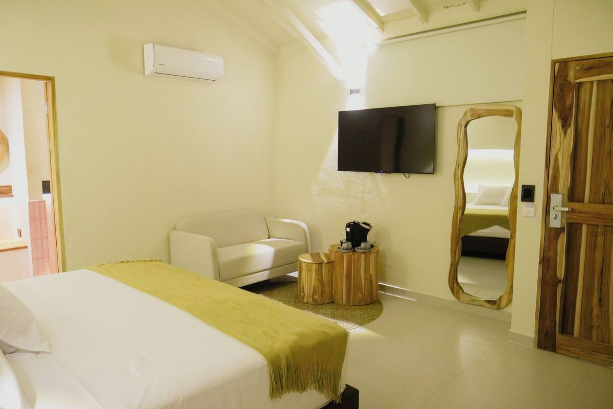 A hotel room with a bed, a sofa, a TV mounted on the wall, and a wooden door.