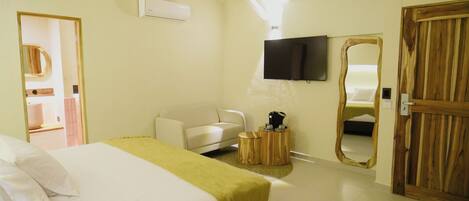 A hotel room with a bed, a sofa, a TV mounted on the wall, and a wooden door.