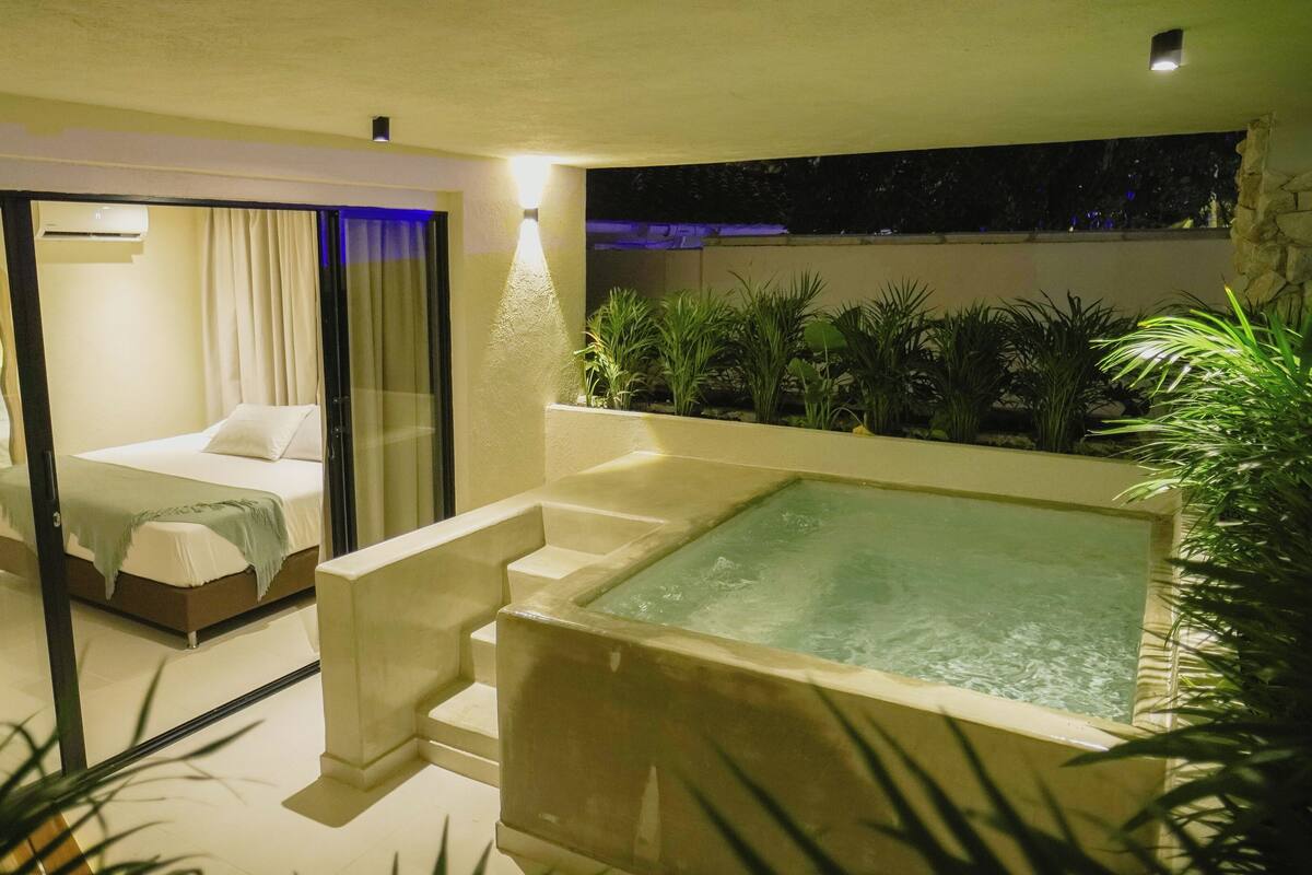 A modern bedroom with a glass door leading to a balcony, a large bathtub, and a view of the night sky.