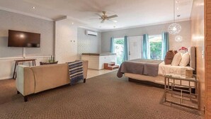 A modern bedroom with a bed, a sofa, a TV, and a ceiling fan. - Luxury Hot tub Suite w/ In-Room Hot Tub & King Bed 1BR, 1BA (Nashville)