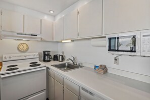 Une cuisine moderne avec des armoires blanches, une cuisinière encastrée, un évier, une machine à café et un four à micro-ondes.