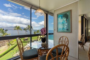 A dining area with a glass table, wicker chairs, and a view of the ocean.