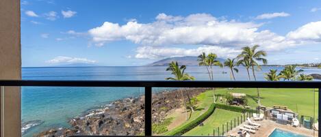 A balcony with a view of the ocean and a pool area.