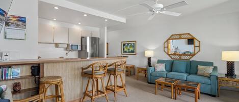 A modern kitchen with a bar area, a teal sofa, and a ceiling fan.
