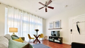 Een woonkamer met een bank, stoelen, een televisie, een plafondventilator en een deur met een paraplu.