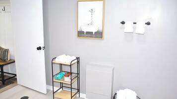 A bathroom with a white door, a framed picture of a bathtub, a towel rack, and a shelf with toiletries.
