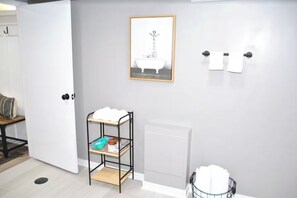 A bathroom with a white door, a framed picture of a bathtub, a towel rack, and a shelf with toiletries. - Walk to the Big House, Sleeps 8, 4 bedrooms, 2 full bathrooms, 3 living rooms  (Ann Arbor)