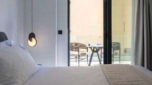 A hotel room with a bed, a hanging light fixture, a sliding glass door leading to an outdoor seating area with chairs and a table. - KEDL Junior Suites 101 (Kalamata)