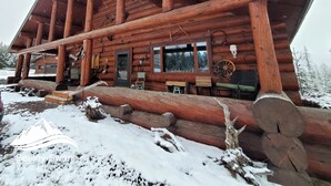 A log cabin with a large porch, wooden beams, and a snow-covered ground. - Log Home close to Hiking Trails! (Seeley Lake)