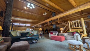 A log cabin interior with a cozy living area, a stone fireplace, and a wooden staircase. - Log Home close to Hiking Trails! (Seeley Lake)