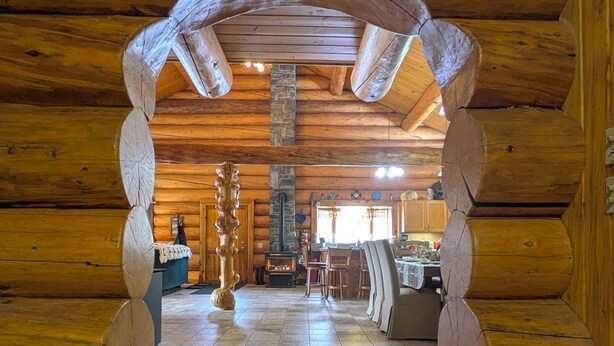 A log cabin interior with a stone fireplace, wooden dining table, and a cozy seating area. - Log Home close to Hiking Trails! (Seeley Lake)