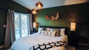Un dormitorio con una cama grande, dos lámparas de noche, un ventanal con cortinas y una decoración de cornamenta de ciervo en la pared.