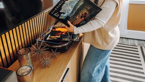 Una persona sosteniendo un libro en una habitación con una mesa de madera, un espejo y una planta.