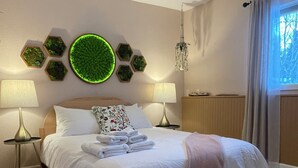 Una cama bien tendida con sábanas blancas, un adorno verde circular en la pared y dos lámparas de noche.