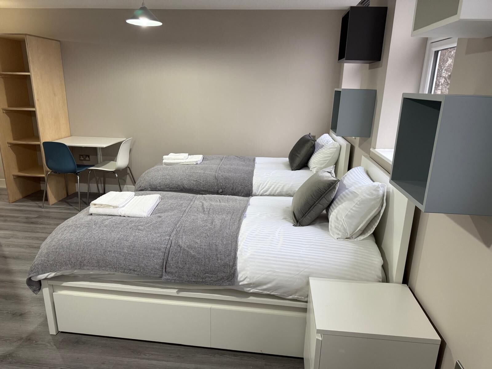 Una habitación de hotel moderna con dos camas, un escritorio, una silla y un televisor.