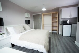 Un dormitorio con cama, mesita de noche y armario con microondas y refrigerador.